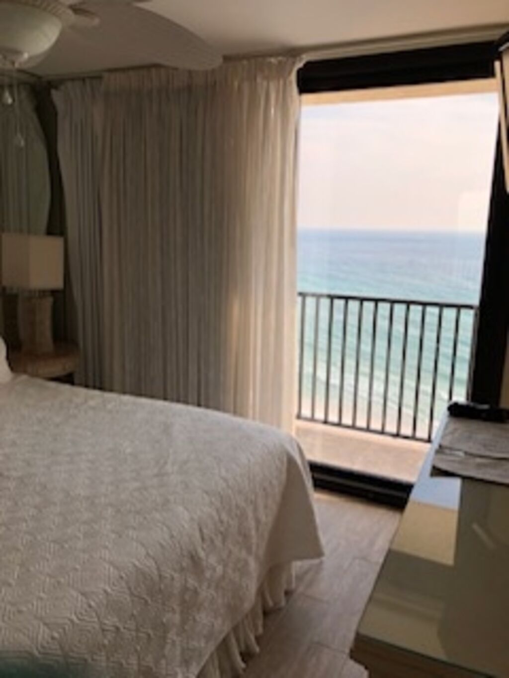 Une chambre d’hôtel avec un grand lit, une table de chevet, une lampe et une vue sur l’océan depuis un balcon.
