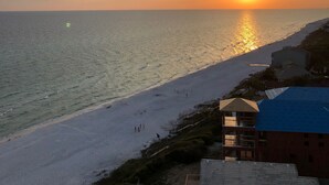 Ein Strand bei Sonnenuntergang, mit blauem Himmel und einigen Gebäuden im Vordergrund.
