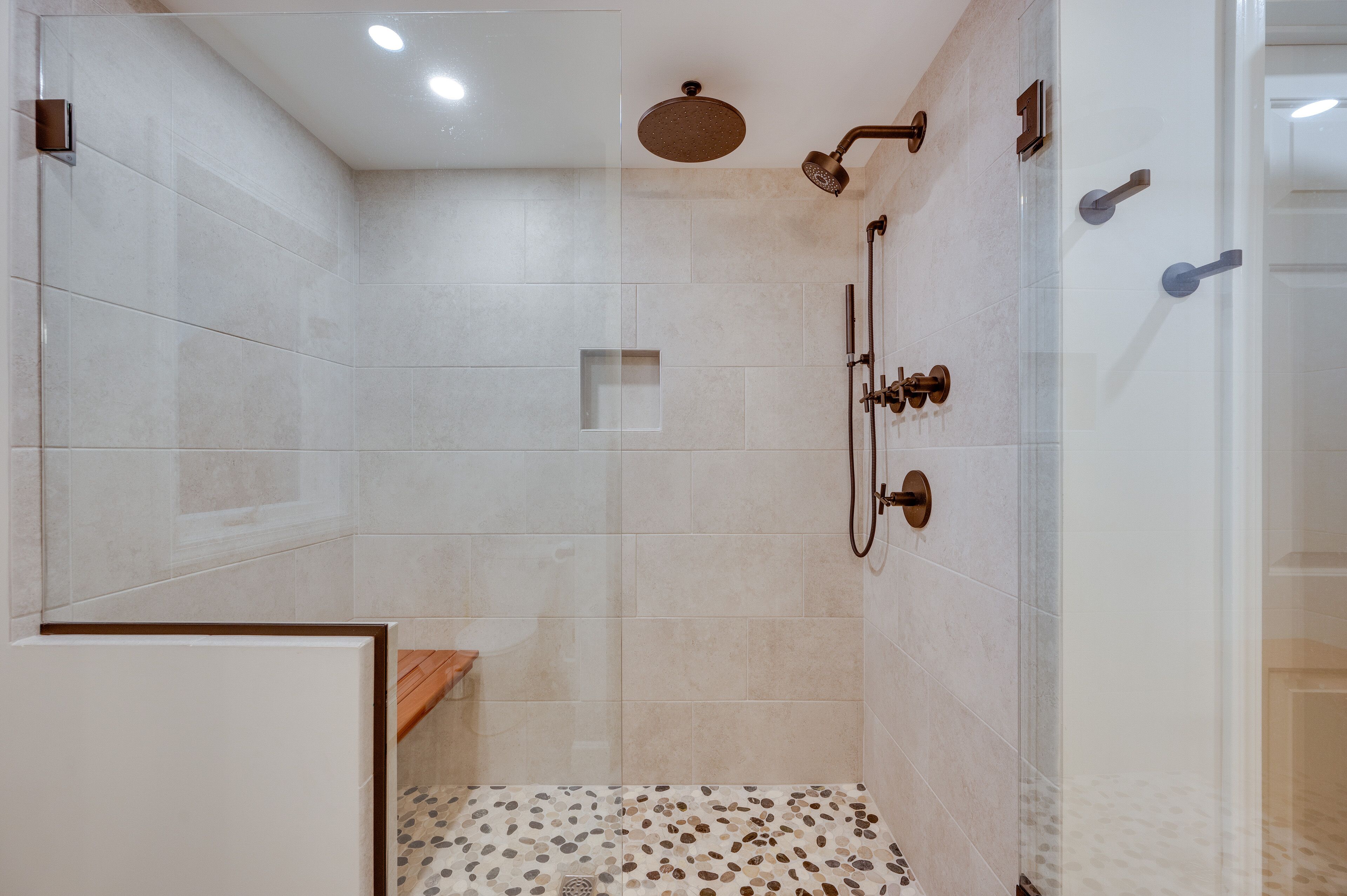 A modern shower area with a rain showerhead, handheld showerhead, and a handheld faucet.