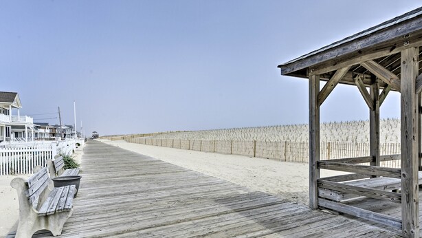 Una pasarela de madera con bancos y una estructura de madera, que conduce a una zona de playa arenosa.