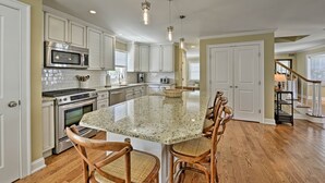 Una cocina amplia con armarios blancos, una isla grande con taburetes de bar, electrodomésticos de acero inoxidable e iluminación colgante.