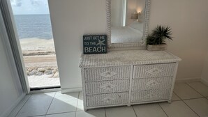Ein Zimmer mit einem großen Spiegel, einem Korbstuhl-Waschtisch, einem Strandschild und Blick auf den Strand.