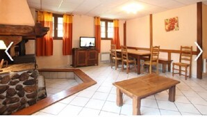Un salon avec une cheminée en pierre, un téléviseur, une table à manger avec des chaises et un banc en bois.