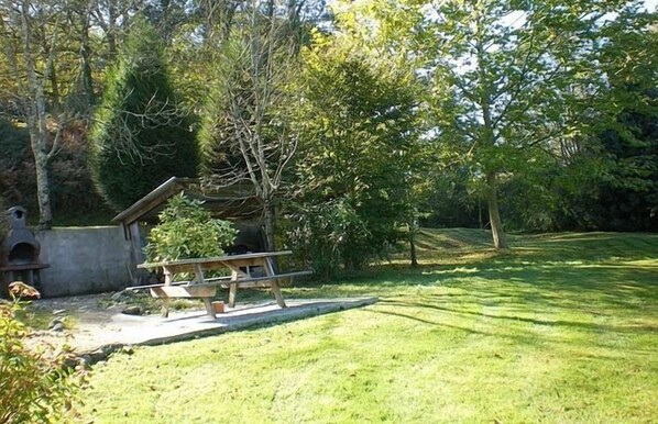 A grassy outdoor area with a picnic table and a small structure, surrounded by trees.