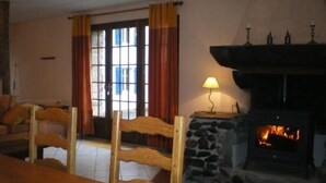 Un salon chaleureux avec une cheminée en pierre, un banc en bois et une vue à travers une porte vitrée.