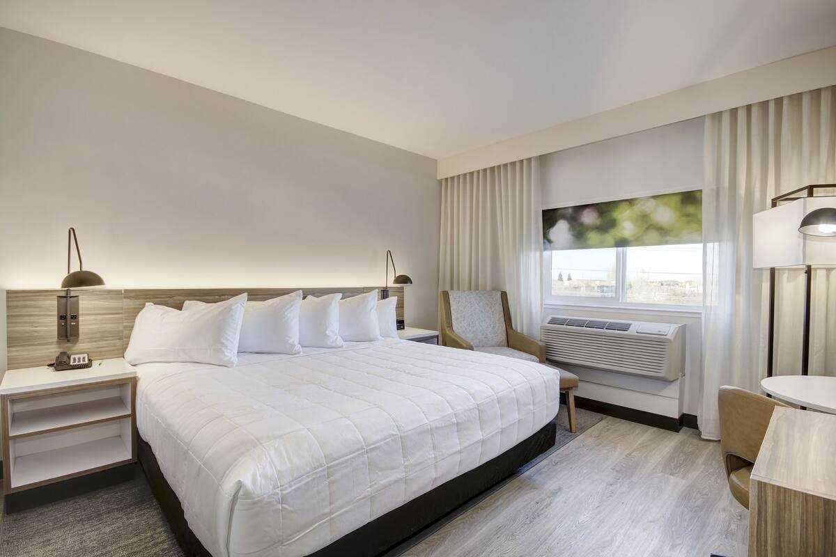 A hotel room with a large bed, bedside tables, a chair, a desk, and a window with curtains.