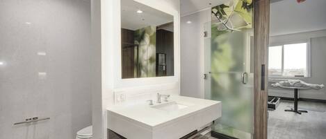 Une salle de bain moderne avec un grand miroir, un lavabo blanc et une cabine de douche en verre.