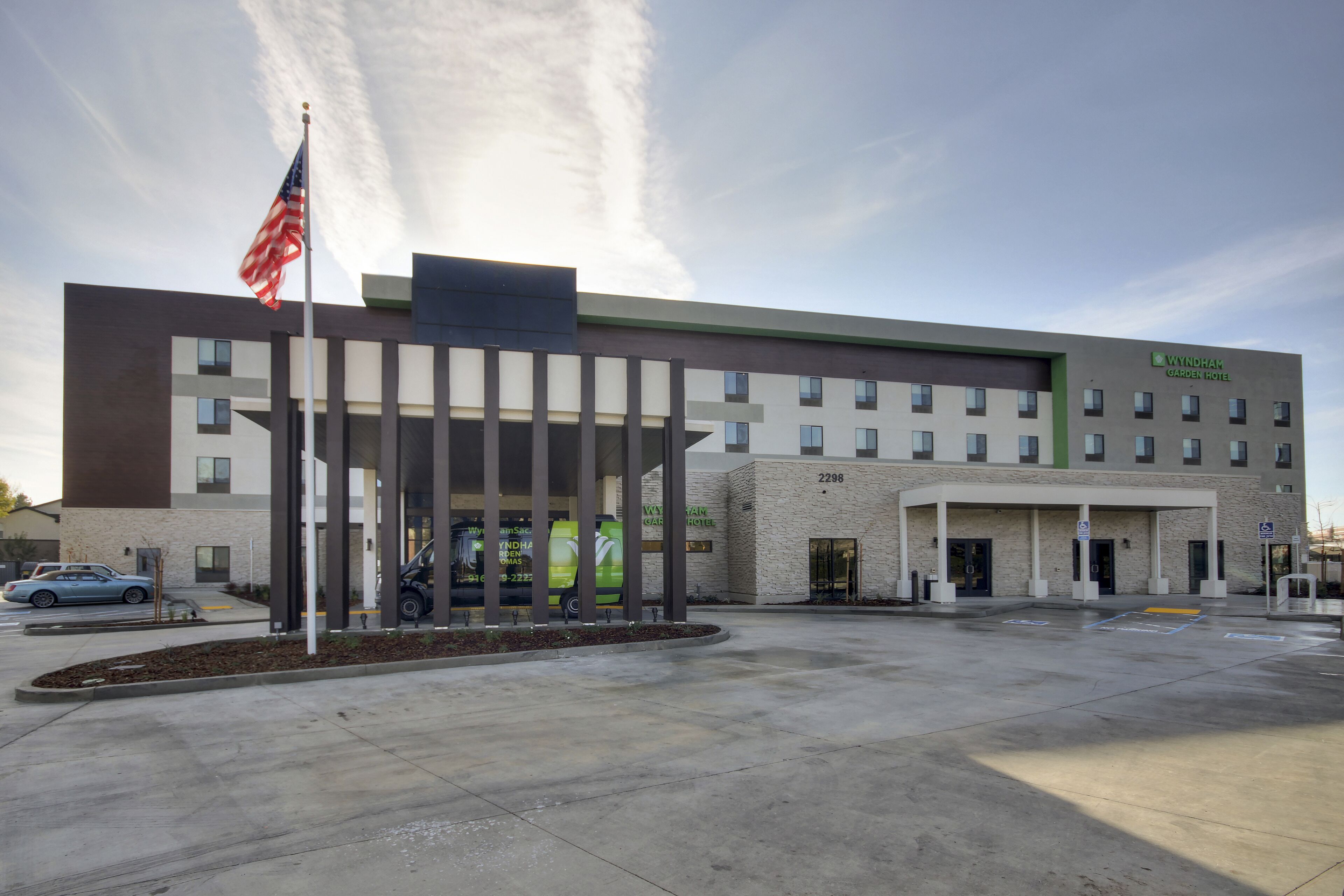 A modern hotel with a prominent entrance, a flag, and a clear sky.
