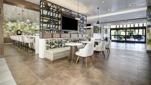 A modern bar area with a large TV, seating, and a view of a vehicle through the glass door. - Wyndham Garden Sacramento Airport Natomas (Sacramento)