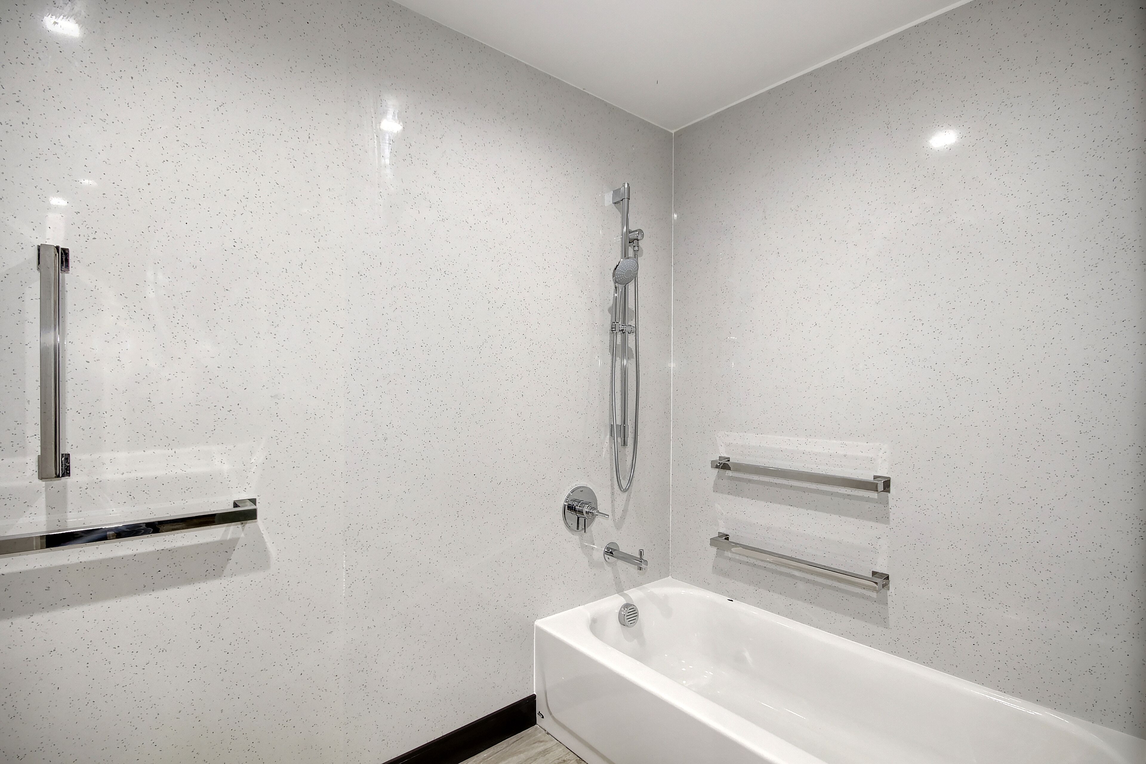 Un baño moderno con pared blanca moteada, una bañera, un cabezal de ducha y un pasamanos.