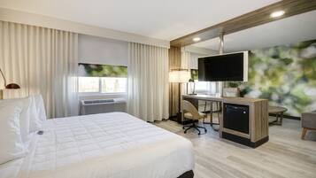 Habitación de hotel con una cama grande, un escritorio con computadora, televisor y ventana con cortinas.