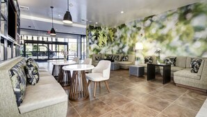 A modern hotel lobby with a seating area, a round table, and a wall with a leafy mural. - Wyndham Garden Sacramento Airport Natomas (Sacramento)