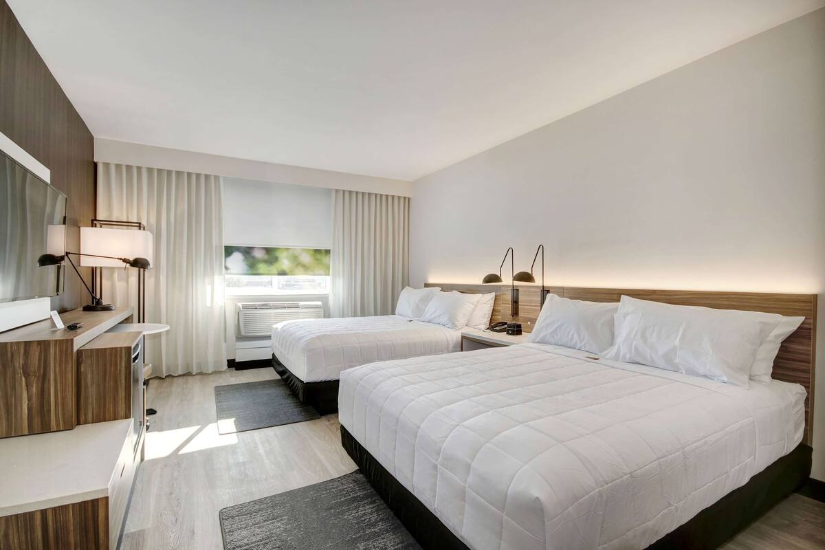A hotel room with two beds, a desk, a mirror, and a window with curtains.