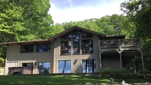 A two-story house with a balcony, large windows, and a stone retaining wall. - 2.8 Acres of Mountain Magic.  Close to Everything.  (Pisgah Forest)