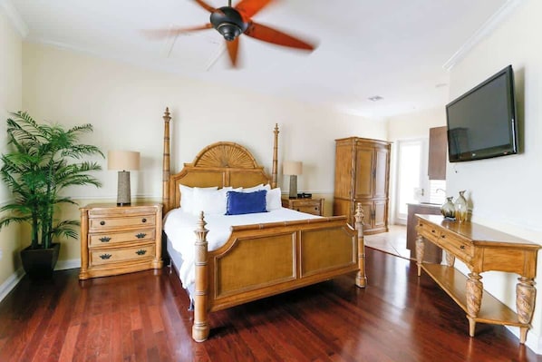 A bedroom with a wooden bed, a nightstand, a dresser, a television, and a ceiling fan.