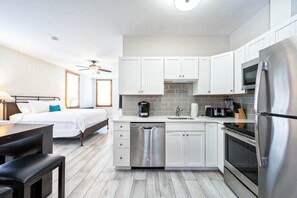 A compact hotel room with a kitchenette, a bed, a dining area, and a ceiling fan.