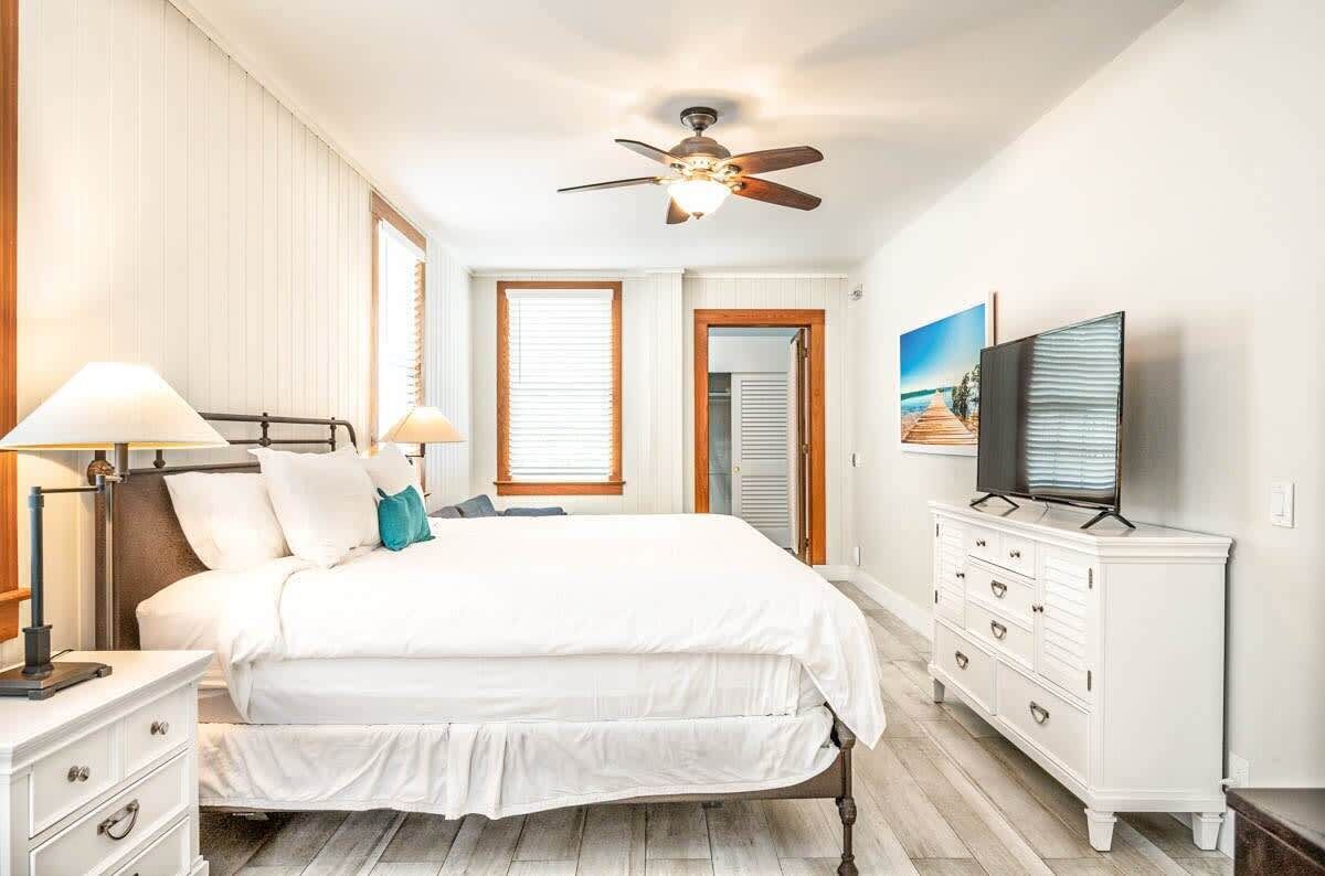 Un dormitorio con cama, lámparas de noche, ventilador de techo, cómoda y televisor.