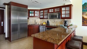 A modern kitchen with granite countertops, stainless steel appliances, and wooden cabinetry. - Penthouse Waipouli Beach Resort E404 - Beautiful Ocean & Pool View (Kapaa)