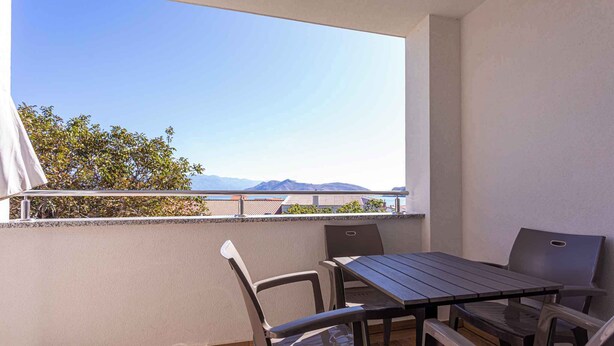 A balcony with a table and chairs, a view of mountains, and a clear sky.