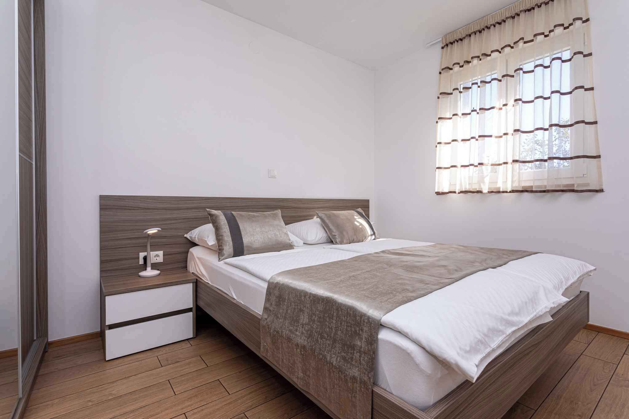 A bedroom with a wooden bed, a bedside table with a lamp, and a window with curtains.