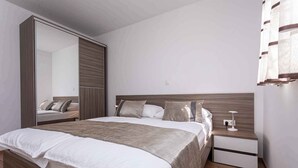 A modern bedroom with a large bed, a nightstand, a mirror, and a wardrobe.