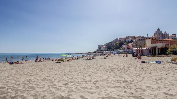 A beach with people sunbathing and swimming, buildings in the background, and a clear sky. - 2 bedroom nice home in Valloria (Valloria)