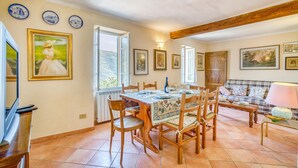 A dining area with a wooden table and chairs, a sofa, and a TV. There are framed pictures on the walls and a window with a view. - 2 bedroom nice home in Valloria (Valloria)