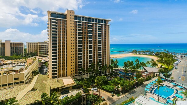 Un hotel moderno con piscina, vista a la playa y jardines tropicales.