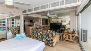 Una habitación de hotel con cama, sofá, televisión, balcón y zona de cocina.