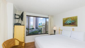 Une chambre d’hôtel avec un lit, une chaise, une fenêtre donnant sur la ville, un tableau au mur et une lampe.