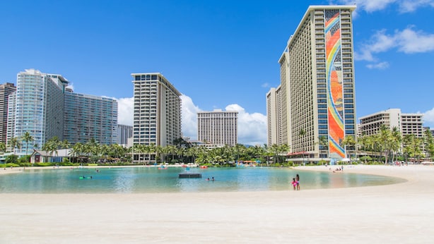 A beachfront hotel with a large pool, palm trees, and high-rise buildings in the background.