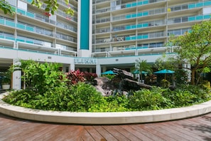 A multi-story hotel with balconies, a central fountain, and lush greenery.
