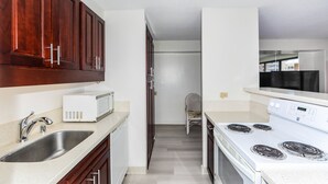 A kitchen with wooden cabinets, a white microwave, a stainless steel sink, and a white stove. - Spacious Studio, Perfect Location In Wakiki, Located Near The Beach, Shopping (Honolulu)