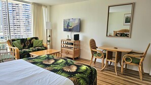 Ett hotellrum med en säng, ett skrivbord, en stol, en tv och ett fönster med utsikt över staden.