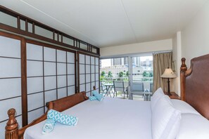 A hotel room with a large bed, a balcony with a table and chairs, and a view of buildings and palm trees.