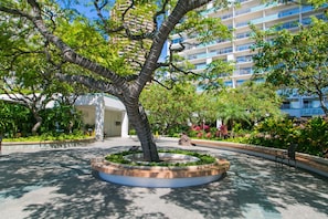A landscaped courtyard with a central tree, a circular seating area, and a multi-story building in the background.