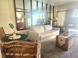 A living room with a sofa, a round table, a wicker chair, a television, and a large mirror.