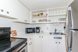 Eine Küche mit weißen Schränken, einer schwarzen Mikrowelle, einem Edelstahl-Kühlschrank und einem Spülbecken mit Armatur.
