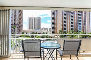 A balcony with two chairs and a round table, overlooking a cityscape with high-rise buildings and palm trees.