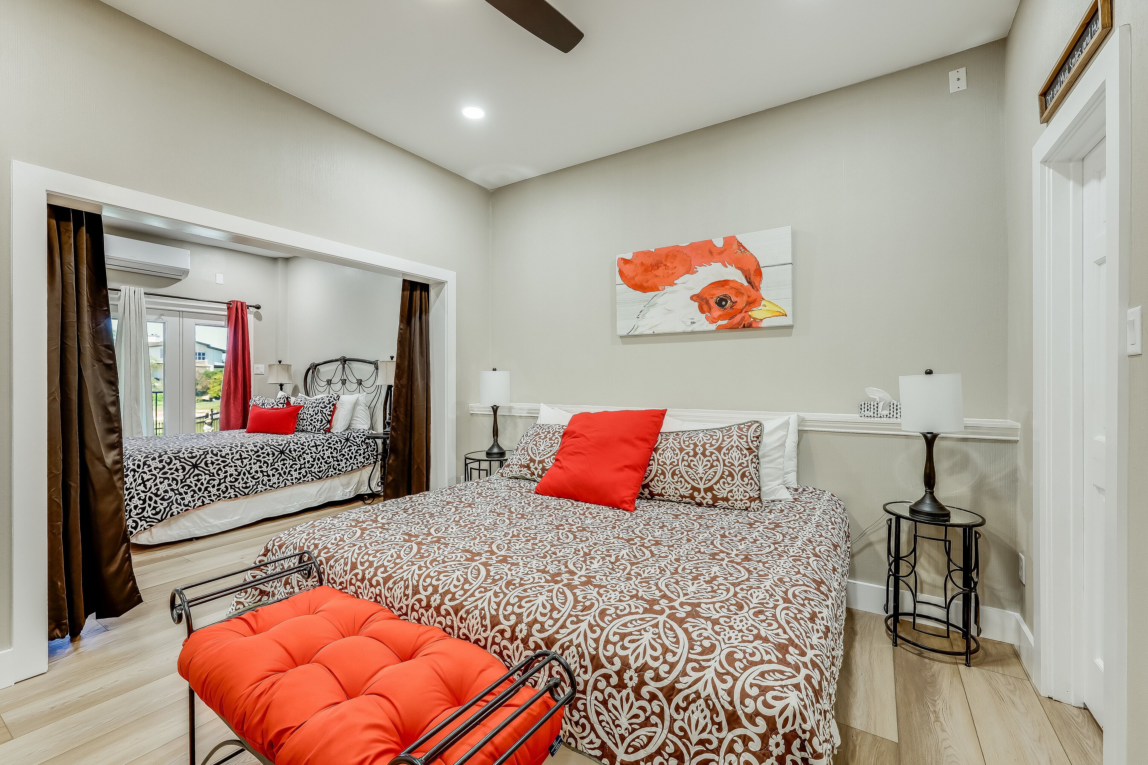 A bedroom with a large bed, a red pillow, a small table, and a wall painting.