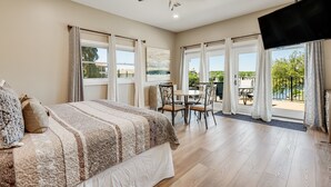 Een slaapkamer met een bed, een plafondventilator, een flatscreen televisie en een balkon met een tafel en stoelen.