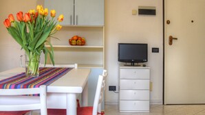 Ein Zimmer mit einem Esstisch, einer Tulpenvase, einem Fernseher auf einem Schrank und einer Tür.