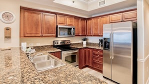 A kitchen with granite countertops, stainless steel appliances, wooden cabinets, and a clock on the wall. - Seawind 402 | Great condo with perfect beach view and walk to dine, shop, more! (Gulf Shores)