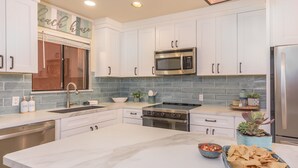 A modern kitchen with white cabinets, a stainless steel refrigerator, a microwave, and a stove. There is a large island with a bowl of salsa and chips. - New! Perfect Location with Great View of Ocean! (San José del Cabo)