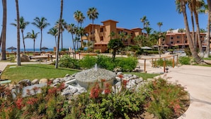 A resort with a pool, palm trees, and a building with multiple balconies. - New! Perfect Location with Great View of Ocean! (San José del Cabo)