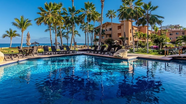 A swimming pool with lounge chairs and palm trees, surrounded by a building with a view of the ocean. - New! Perfect Location with Great View of Ocean! (San José del Cabo)