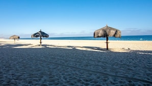A beach with three thatched umbrellas and a clear blue sky. - New! Perfect Location with Great View of Ocean! (San José del Cabo)