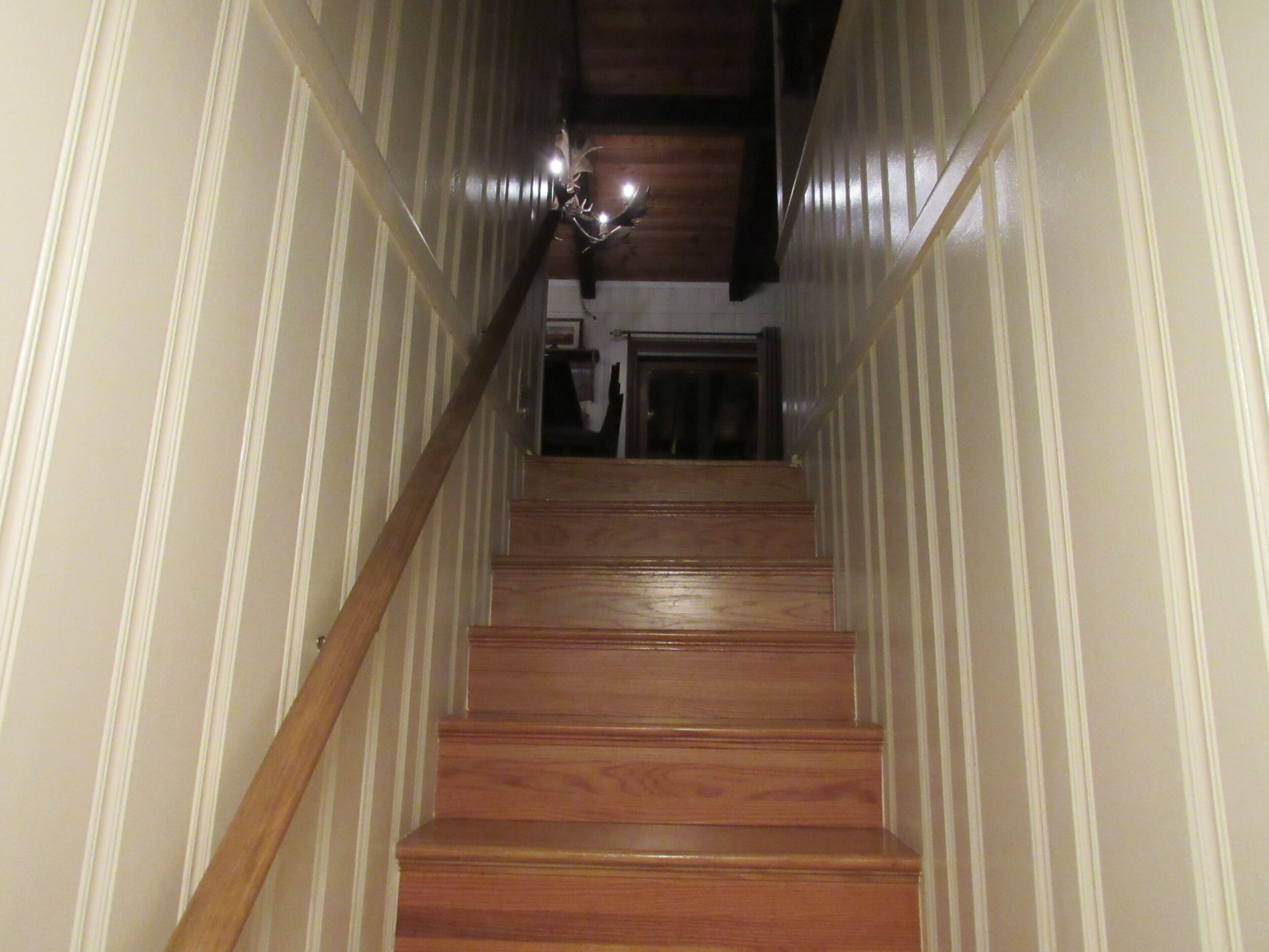 A wooden staircase with white paneling on the walls, leading to a landing with a door and a light fixture.