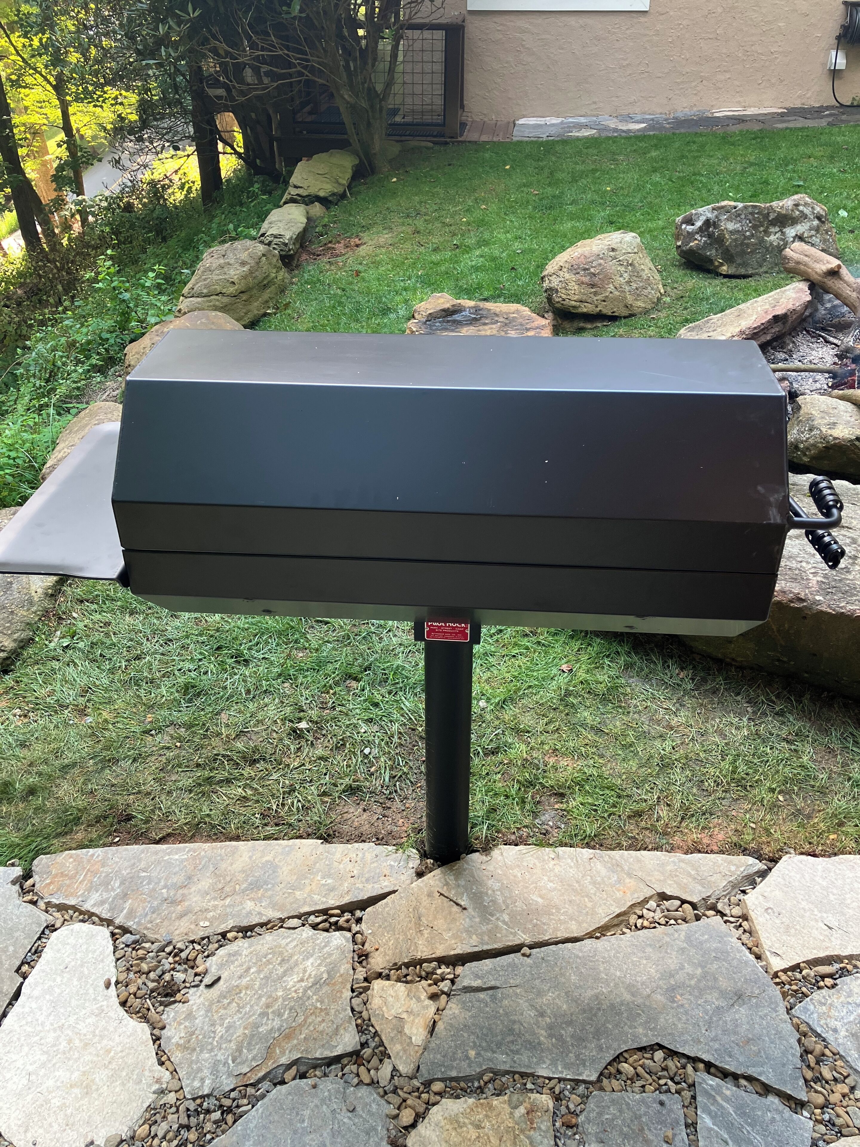 A black outdoor grill on a stone patio with a grassy yard and a house in the background.
