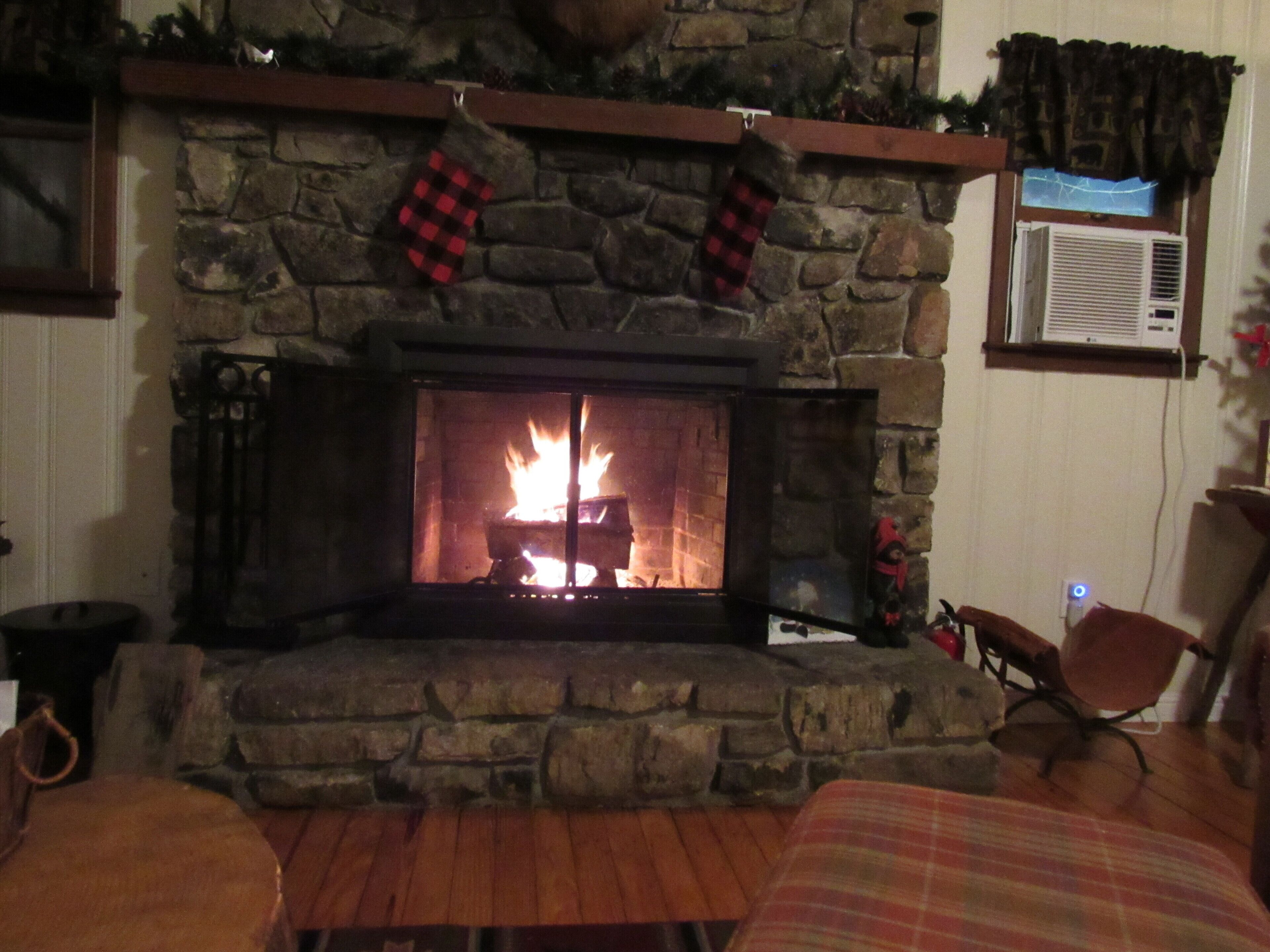 A stone fireplace with a fire, a stone mantle, and a window with an air conditioner.